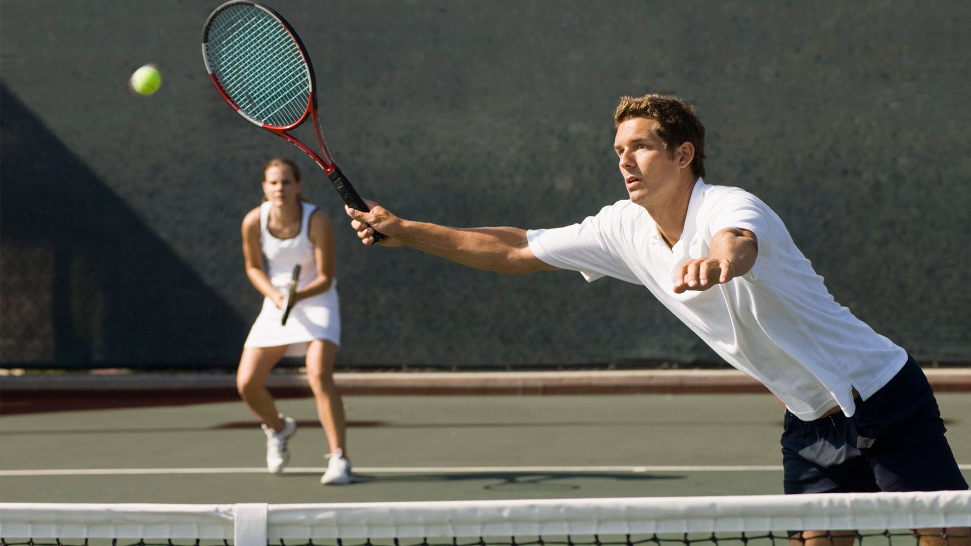 Mixed doubles tennis players with male reaching to hit a ball